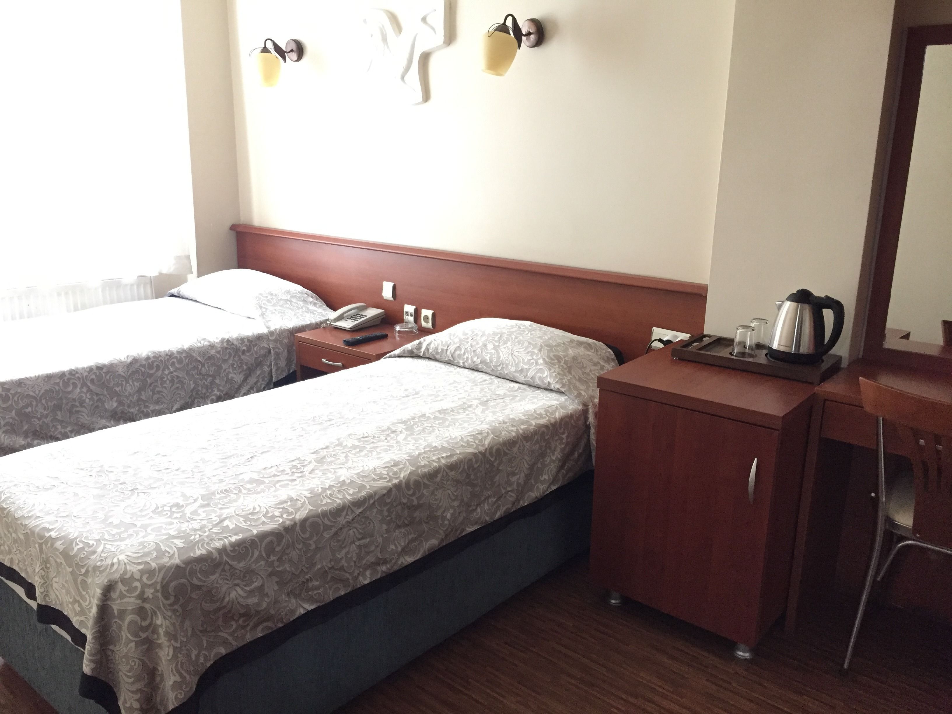 A hotel room with two beds, a wooden desk, a telephone, a kettle, and a mirror.
