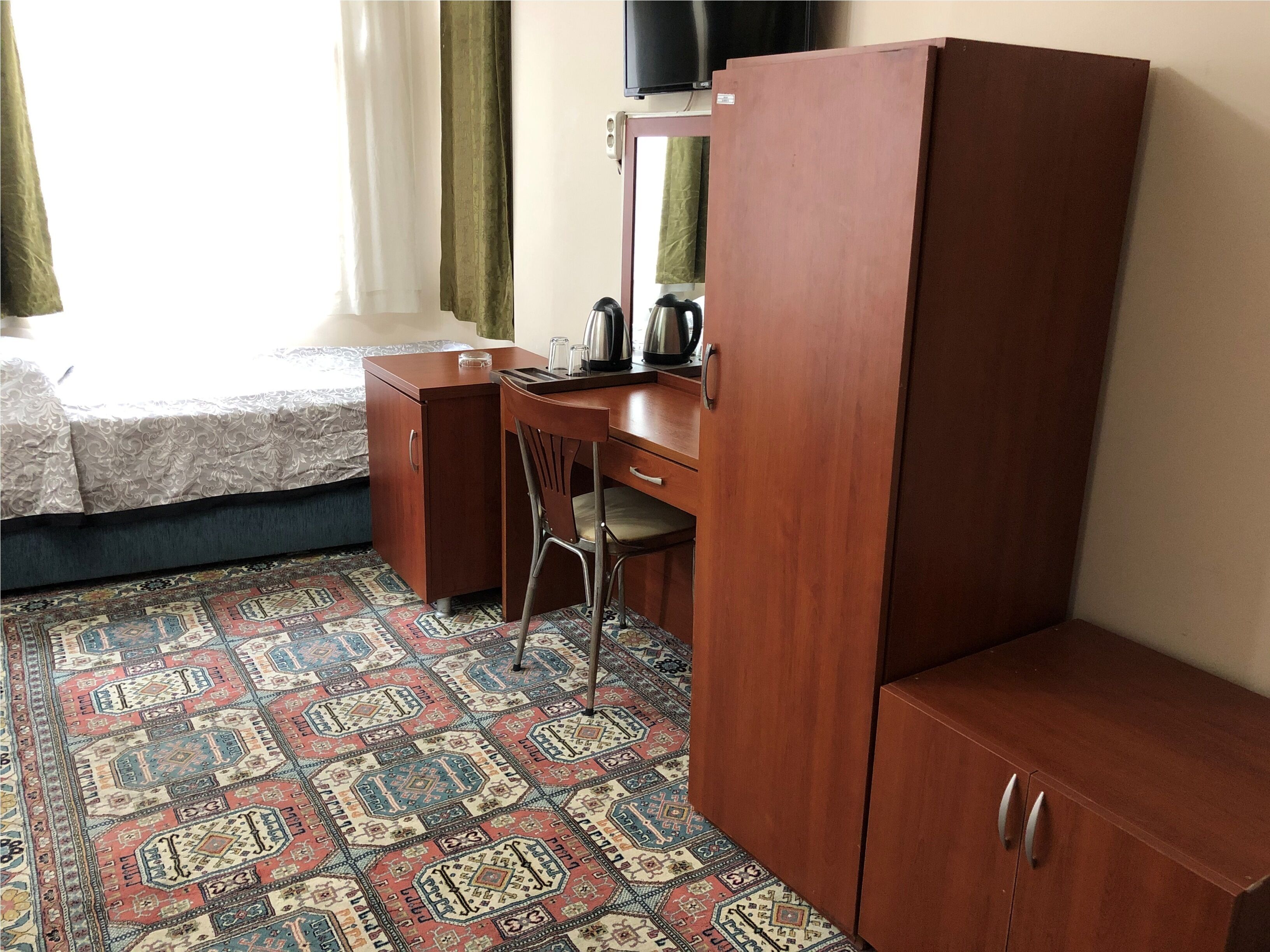 Une chambre d’hôtel avec un lit, un bureau, une armoire et une moquette à motifs.