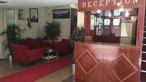 Un área de recepción con alfombra roja que lleva a un mostrador, sofás rojos y plantas en macetas.