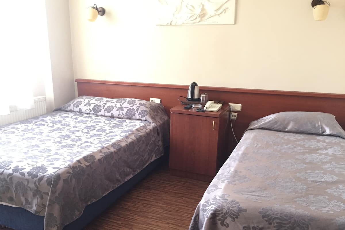 A hotel room with two beds, a wooden nightstand, a telephone, a kettle, and a wall-mounted light fixture.