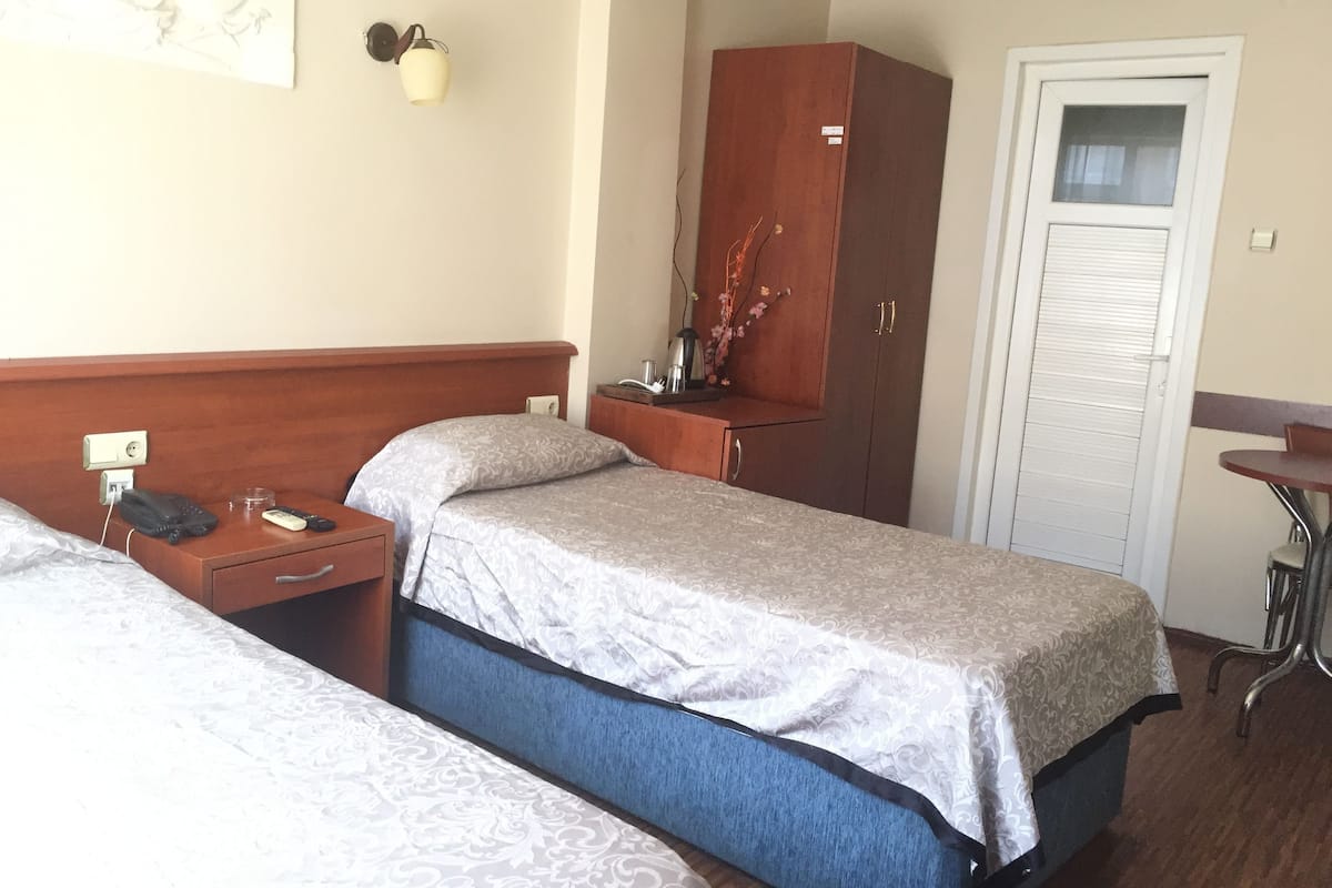A hotel room with two single beds, a wooden wardrobe, a desk with a lamp, and a small table with a chair.