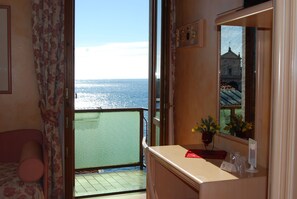 A room with a balcony overlooking the sea, a bed, a small table with a vase of flowers, and a mirror reflecting a building. - Garda Sol Apart-hotel Beauty & SPA (Toscolano Maderno)