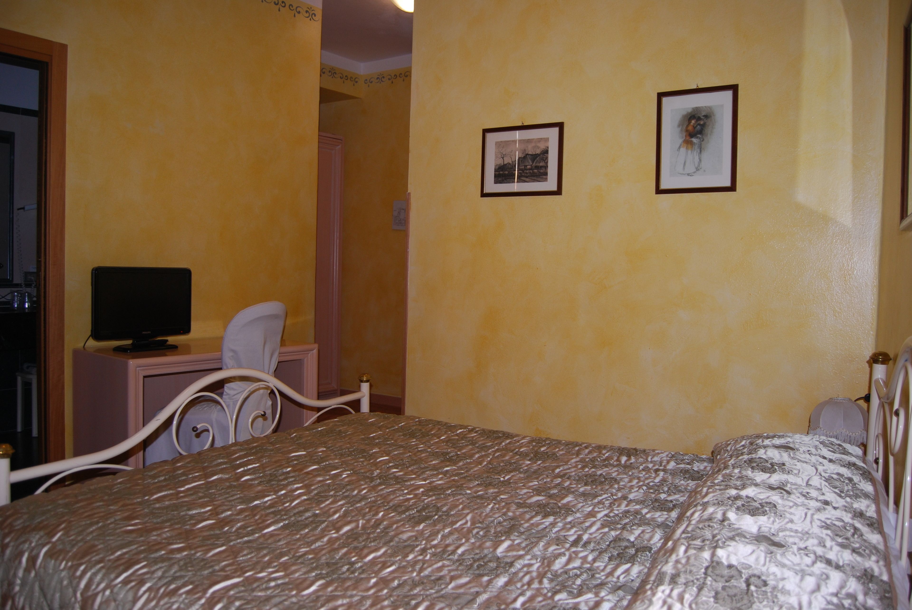 A bedroom with a bed, a television on a desk, and two framed pictures on the wall.
