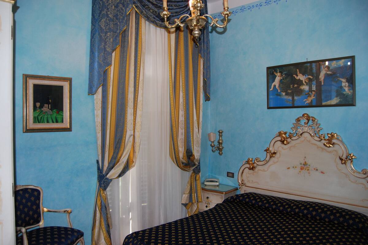 A bedroom with a bed, a chair, a nightstand, a lamp, and a painting on the wall.