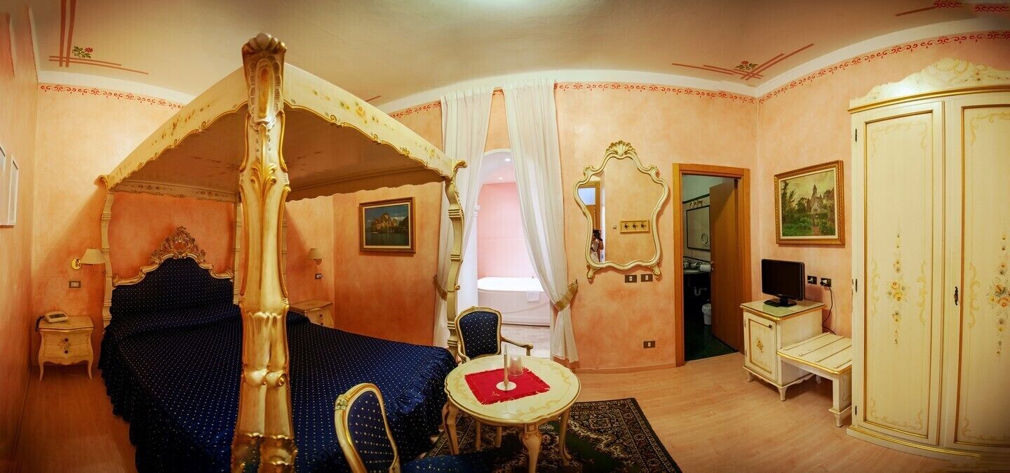Una habitación con cama con dosel, una mesita con mantel rojo, un espejo, un armario y un televisor.