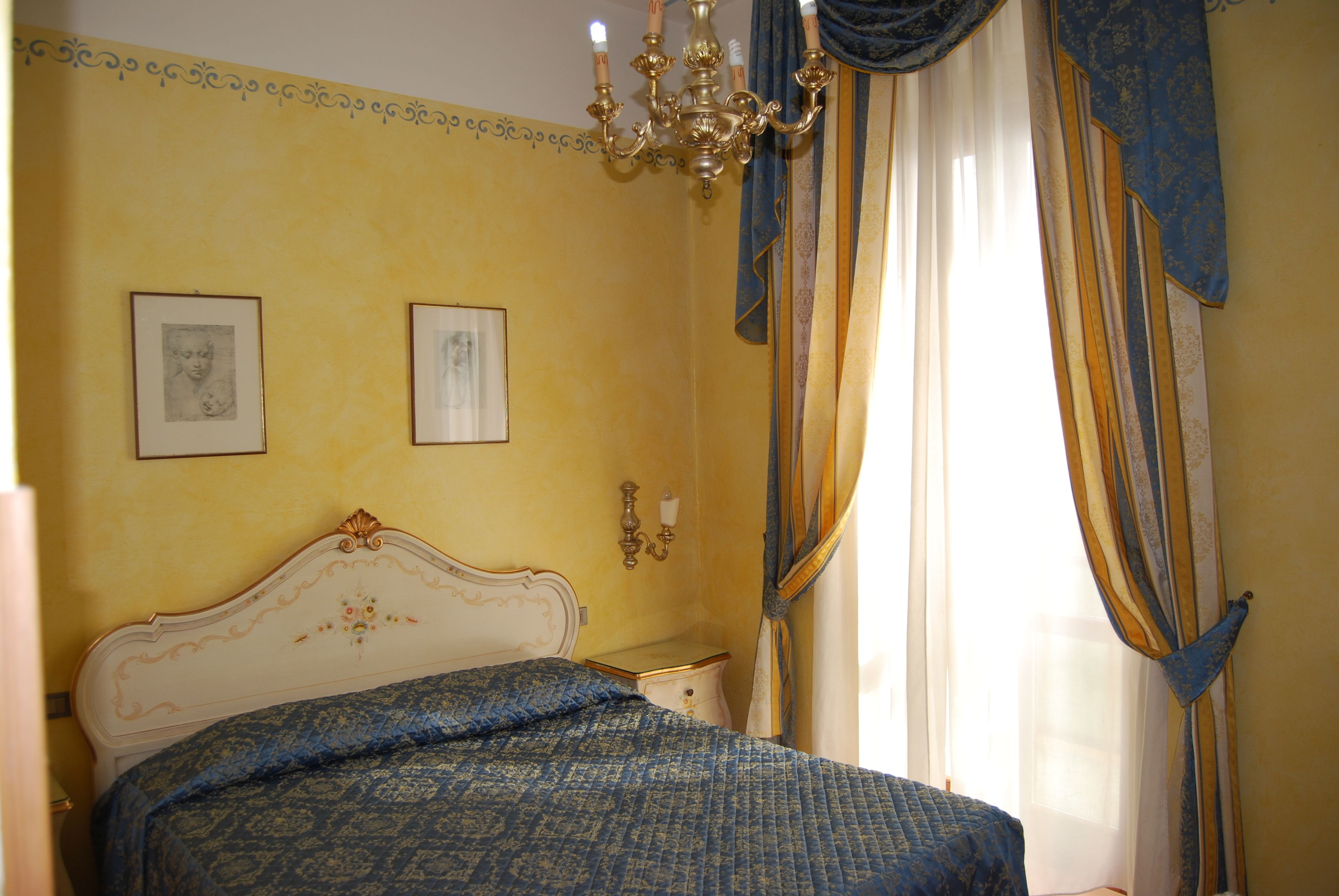 A bedroom with a bed, a chandelier, and curtains.