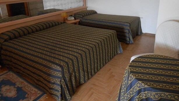 Una habitación con tres camas, cabecero de madera, una mesita de noche y una pequeña mesa con lámpara.
