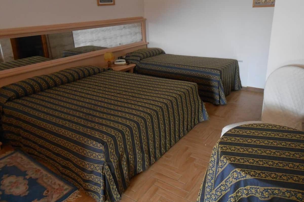A room with three beds, a wooden headboard, a nightstand, and a small table with a lamp.