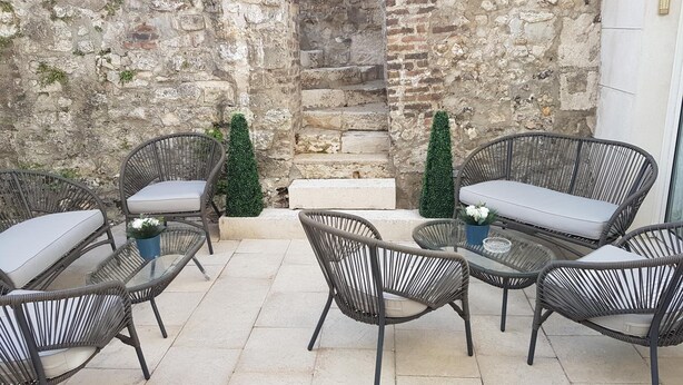 A patio with wicker furniture, stone walls, and small potted plants. - Hotel de la Tour (Pont-de-L'Arche)
