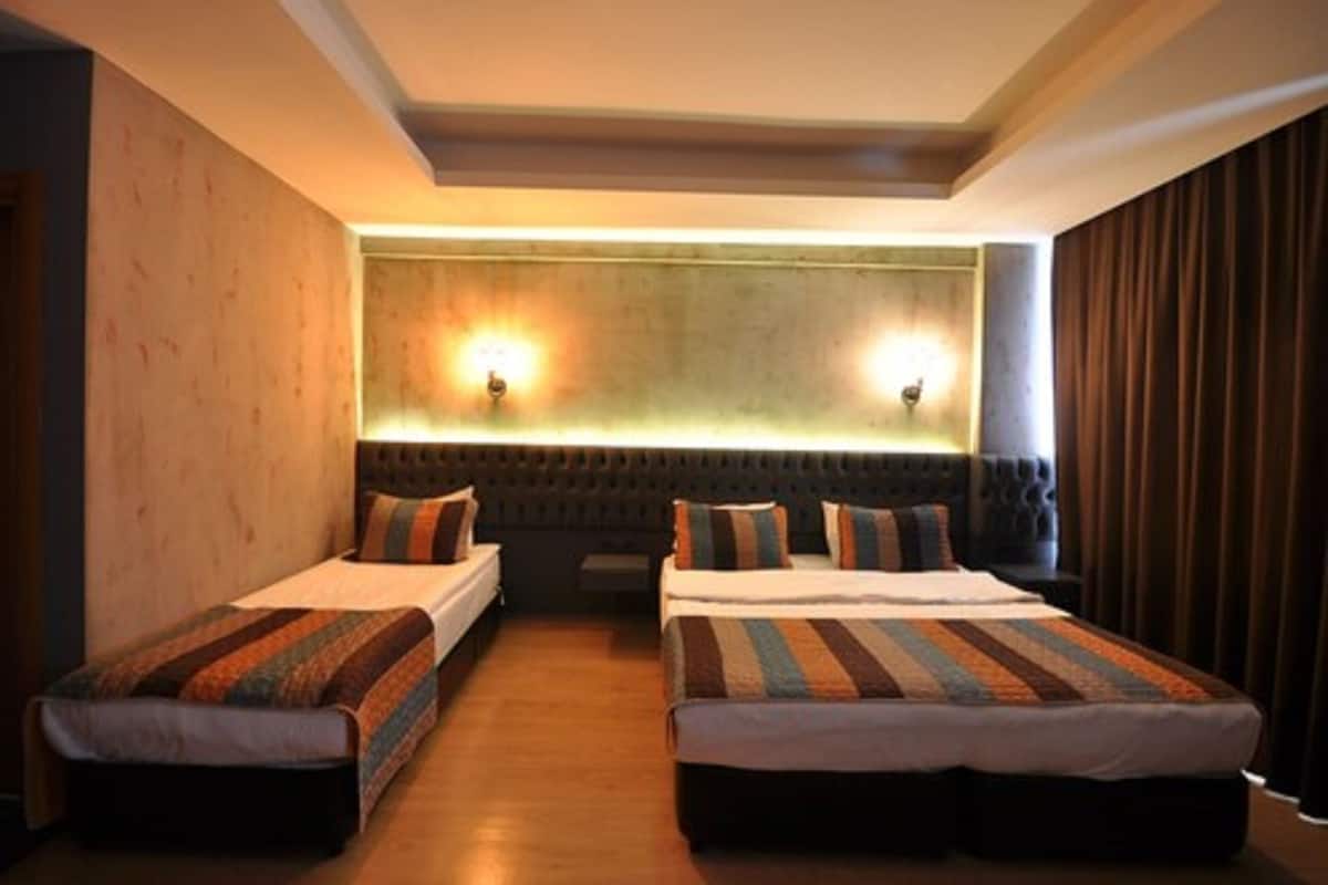 A hotel room with two single beds, a padded headboard, and a wall-mounted light fixture.