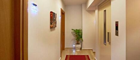 A hallway with a red carpet, a potted plant, and a door with a digital display.