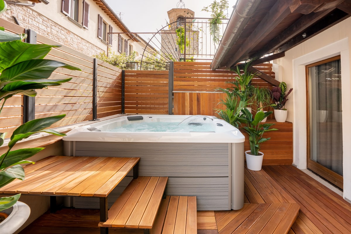 A wooden deck with a hot tub, wooden benches, and potted plants.