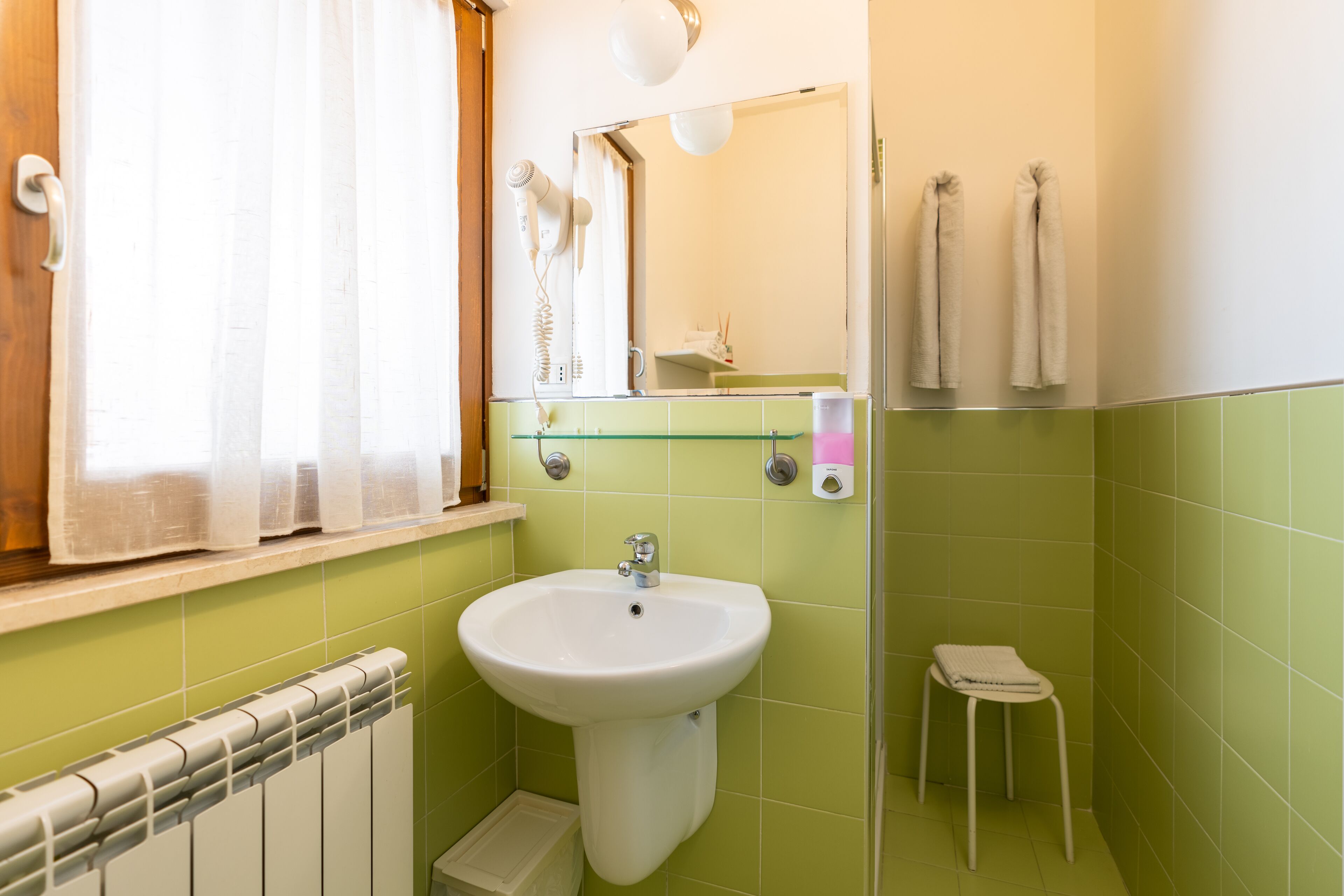 A bathroom with a white sink, green tiles, a mirror, a towel rack, and a radiator.