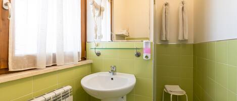 A bathroom with a white sink, green tiles, a mirror, a towel rack, and a radiator.
