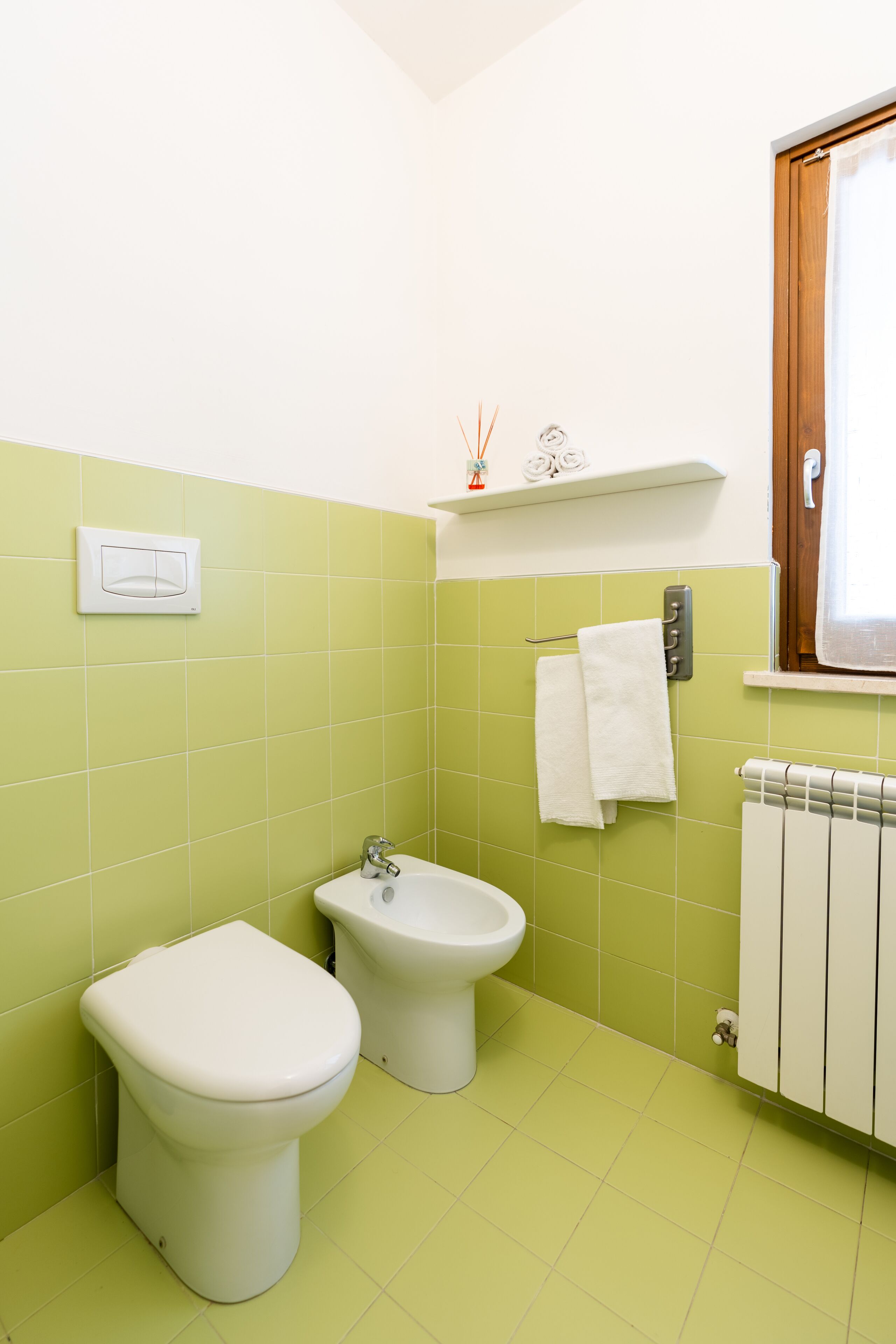 A bathroom with green tiles, a toilet, a bidet, and a radiator.