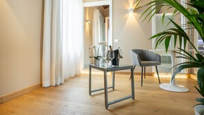 A modern room with a wooden floor, a glass table with a vase of flowers, a chair, and a potted plant. - GG8 Hotel & Suite SPA (Gualdo Tadino)