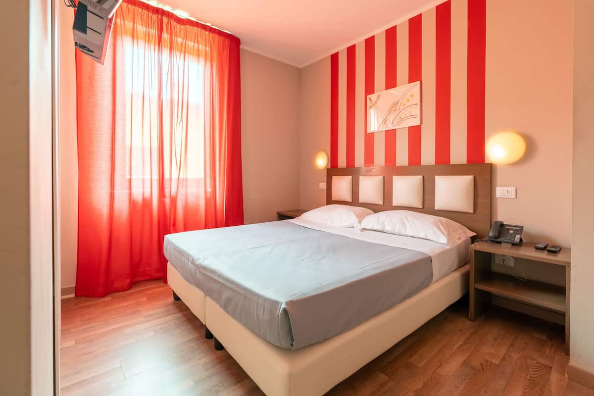A bedroom with a bed, a nightstand, a telephone, and a wall with a striped pattern.