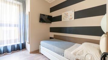 Un dormitorio con cama, televisor montado en la pared, un cuadro y una ventana con cortinas.