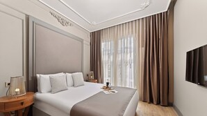 A hotel room with a large bed, a bedside table with a lamp, a TV mounted on the wall, and a window with curtains. - Taksim Premium Residence (Istanbul)