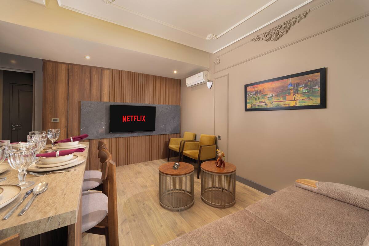 Un soggiorno moderno con una TV a schermo piatto, pareti rivestite in legno, un'area pranzo con tavolo apparecchiato per quattro persone e un divano.