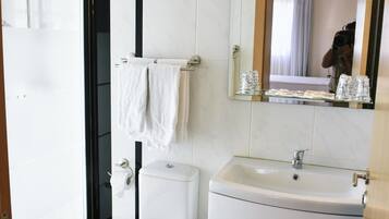 Um banheiro moderno com box de vidro, vaso sanitário branco, pia com espelho em cima e porta-toalhas.