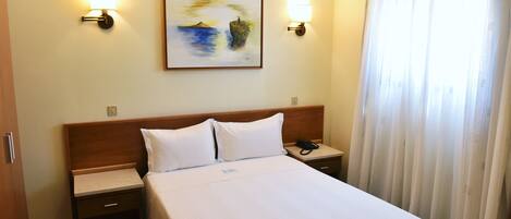 Una habitación de hotel con una cama bien hecha, dos mesitas de noche con lámparas, un cuadro en la pared y una ventana con cortinas.