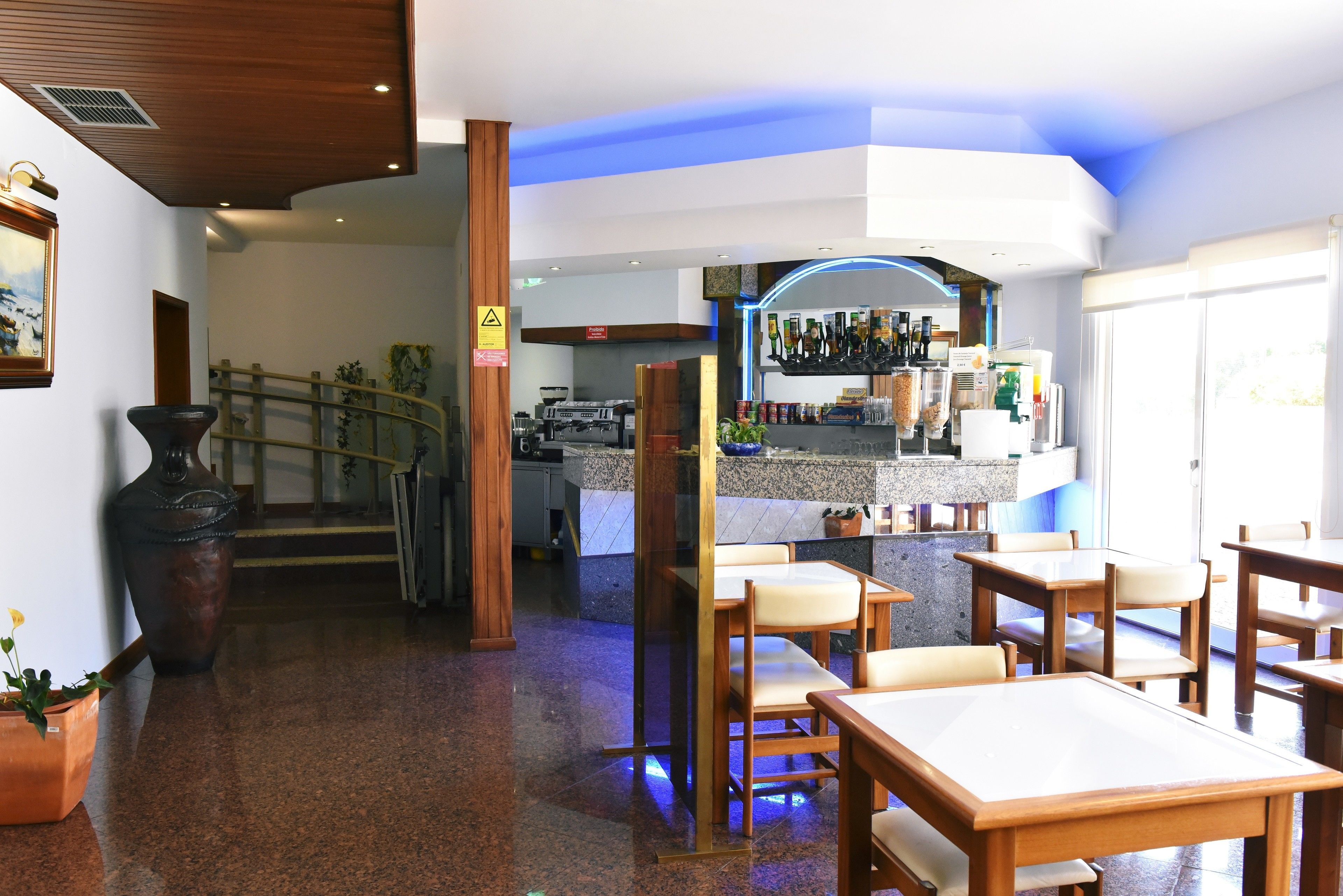 A restaurant with wooden tables and chairs, a bar area with bottles, and a staircase leading to another floor.