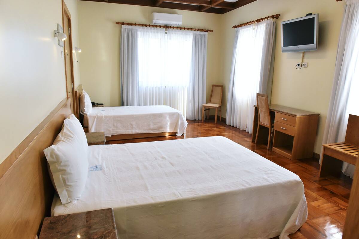A hotel room with two beds, a desk, a chair, a television, and curtains.