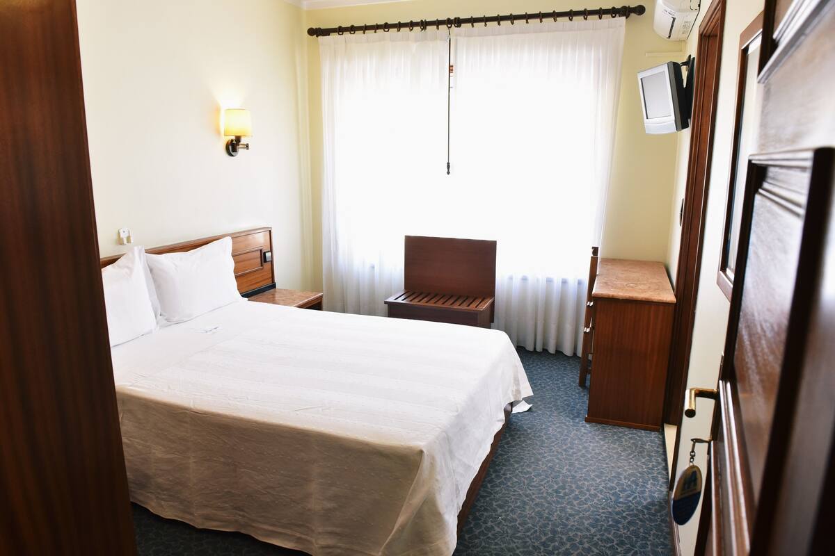 A hotel room with a large bed, a desk, a chair, a television, and a window with curtains.