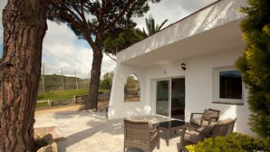 Un edificio blanco con un patio amueblado con mobiliario de mimbre y un ventanal que da al interior.
