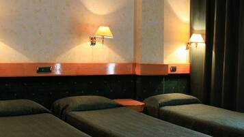 Una habitación de hotel con dos camas individuales, cabecero de madera, dos lámparas fijadas a la pared y una mesita de noche de madera.