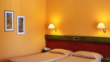 Habitació d'hotel amb dos llits, un capçal vermell, dues làmpades penjades a la paret i dues fotografies emmarcades.