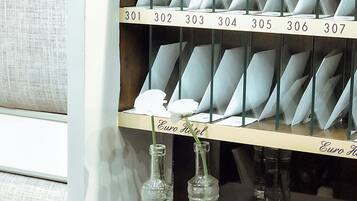 A hotel room with a minibar containing numbered bottles and a flower arrangement.