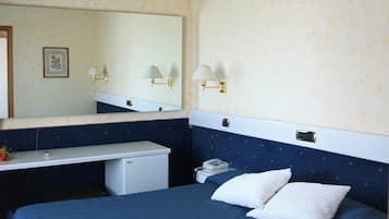 A hotel room with a bed, a small desk with a telephone, a mirror, and wall-mounted lamps.