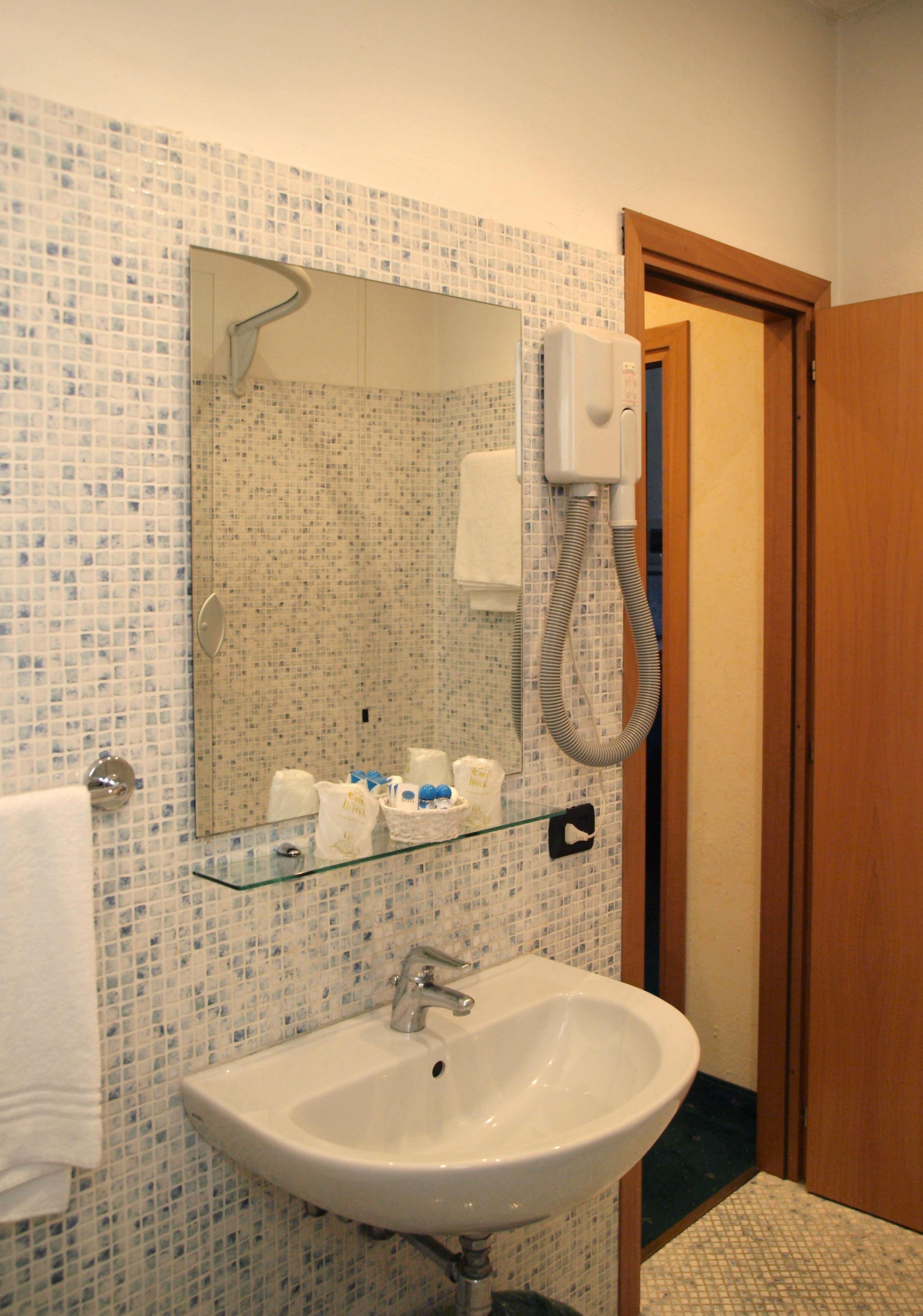 A bathroom with a white sink, a glass shelf with toiletries, a mirror, and a shower head.