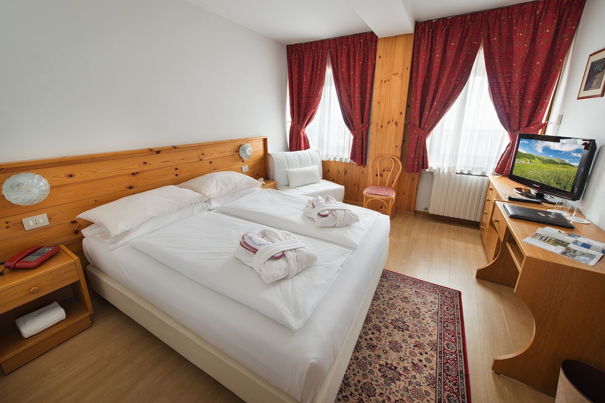 A hotel room with a large bed, wooden headboard, a desk with a computer, a chair, and a television.
