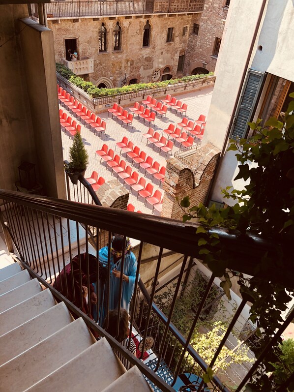 A courtyard with red chairs arranged in rows, a staircase leading down, and a building with arched windows in the background. - Le Suite Di Giulietta (Verona)