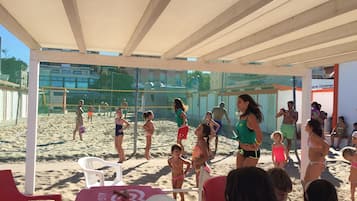 Una cancha de voleibol de playa con espectadores sentados bajo una zona sombreada.