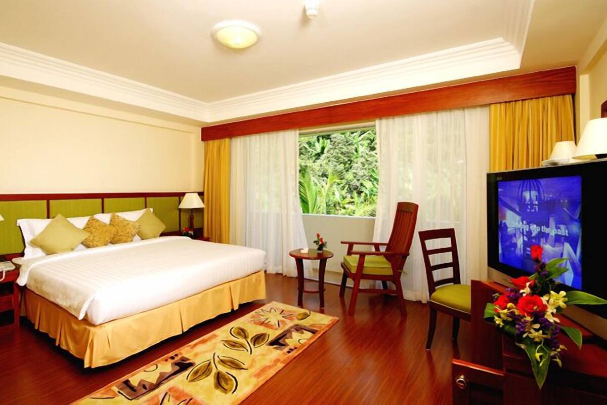 A hotel room with a large bed, a television, a desk with a chair, and a window with curtains.