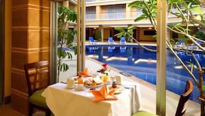 A dining area with a table set for two, overlooking a pool and a building with balconies. - Kalim Resort (Patong)