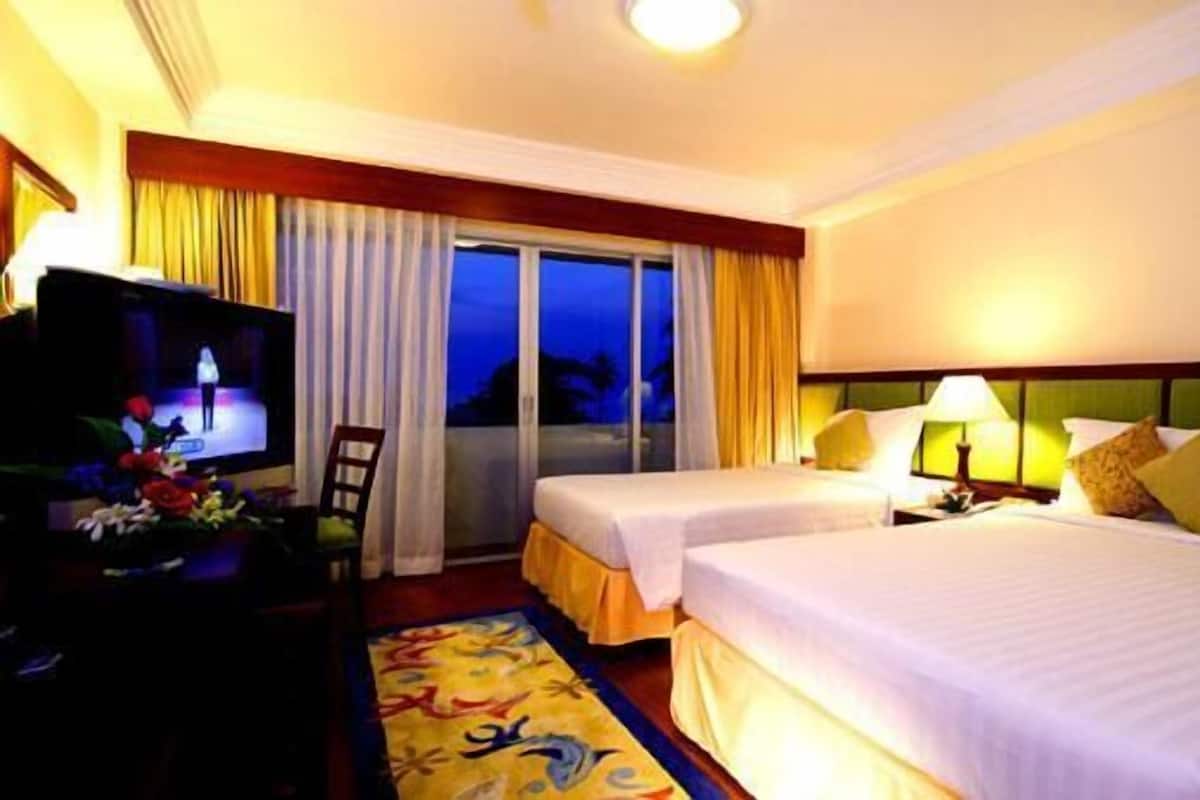 A hotel room with two beds, a television, a desk, and a window with curtains.