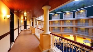 A hotel corridor with multiple balconies, wooden columns, and a view of the surrounding landscape. - Kalim Resort (Patong)