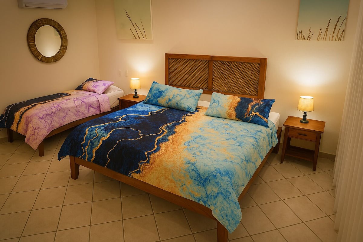 Habitación de hotel con dos camas, cada una con una colcha de diseño único, cabeceros de madera, lámparas de noche y un espejo en la pared.