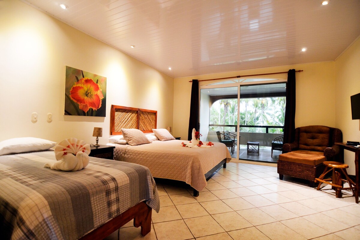 A hotel room with two beds, a balcony, a chair, and a table.