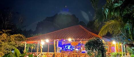 A night-time view of a building with a tiled roof, surrounded by lush greenery and a small pond.