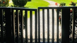Blick von einer Veranda mit Schaukel auf einen gepflegten Garten mit Palmen und einem klaren Himmel.