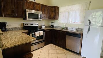A kitchen with wooden cabinets, stainless steel appliances, a granite countertop, and a tiled floor.