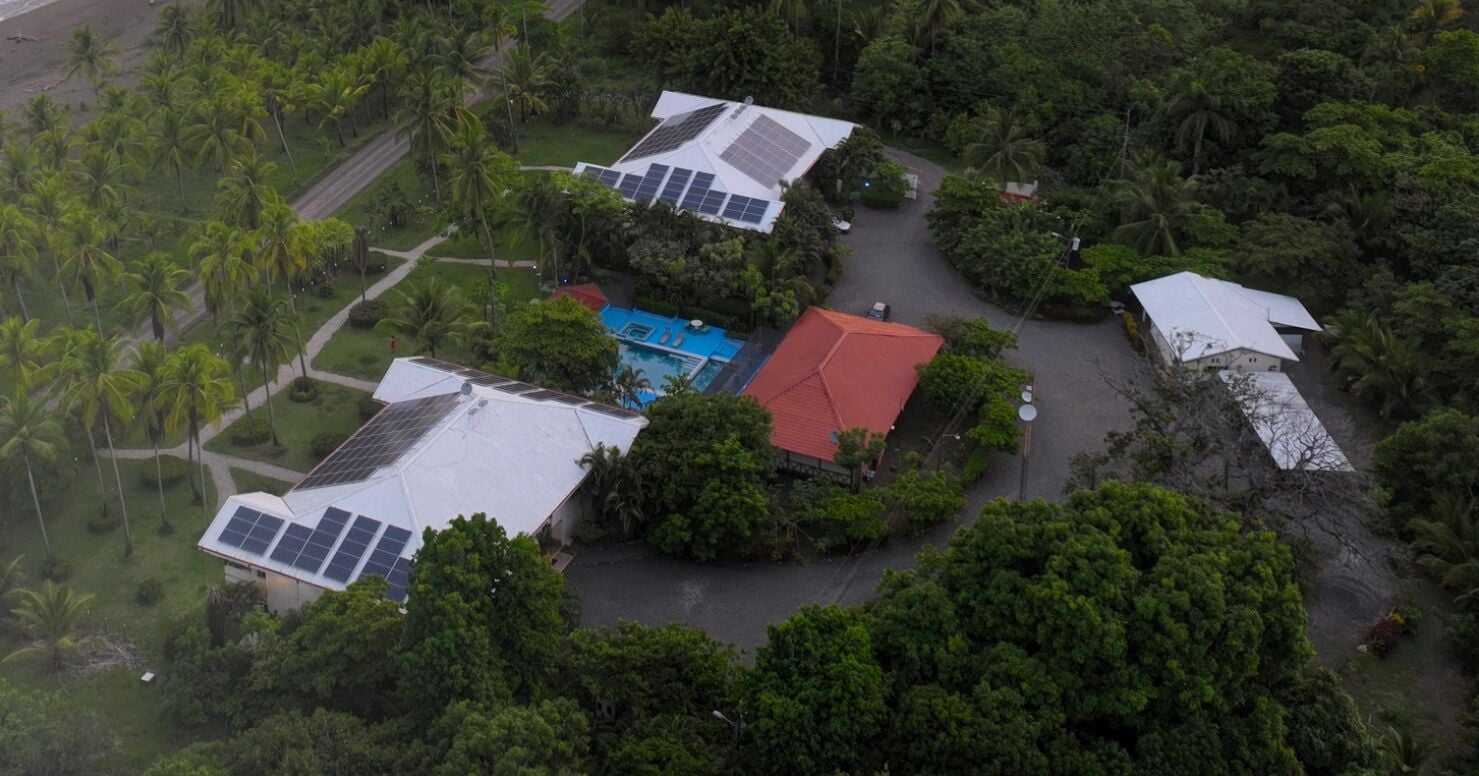 An aerial view of a residential area with multiple houses, solar panels, and a swimming pool.