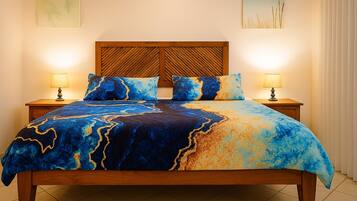 Una cama con una colcha de diseño azul y dorado, cabecera de madera, dos lámparas de noche y una mesita de noche.