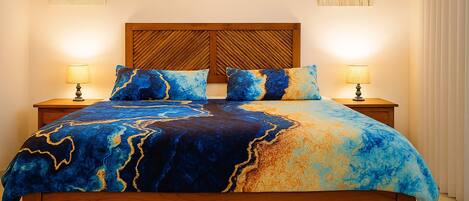 A bed with a blue and gold patterned bedspread, wooden headboard, two bedside lamps, and a nightstand.